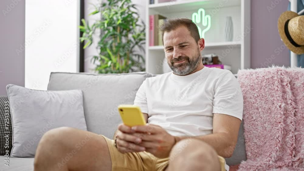 A middle-aged man with grey hair smiles while using a smartphone on a sofa at home, representing a casual lifestyle. A middle-aged man with grey hair smiles while using a smartphone on a sofa at home, representing a casual lifestyle.