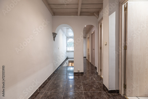 Corridor of residential house with white oak wooden doors, glossy dark stoneware floors