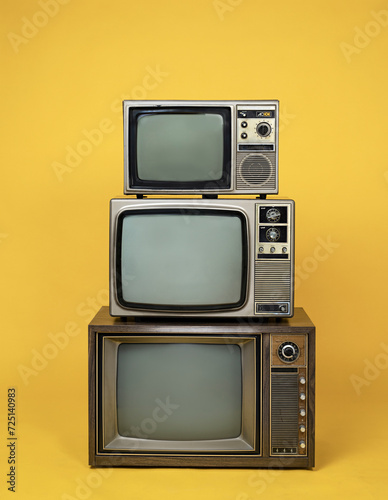 Antique retro old televisions pile on yellow floor. Vintage style. Three old TVs isolated over yellow background.
