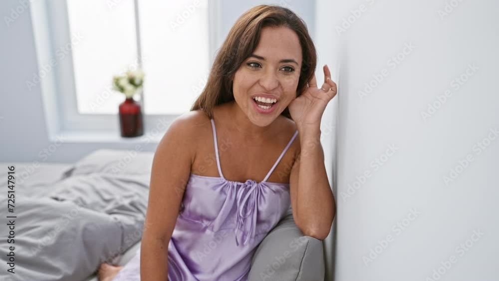 Beauty in bedtime whispers! young hispanic woman in pyjama sitting on bed, hand cupping ear, listening to juicy rumor. navigating deafness in bedroom gossip sessions.