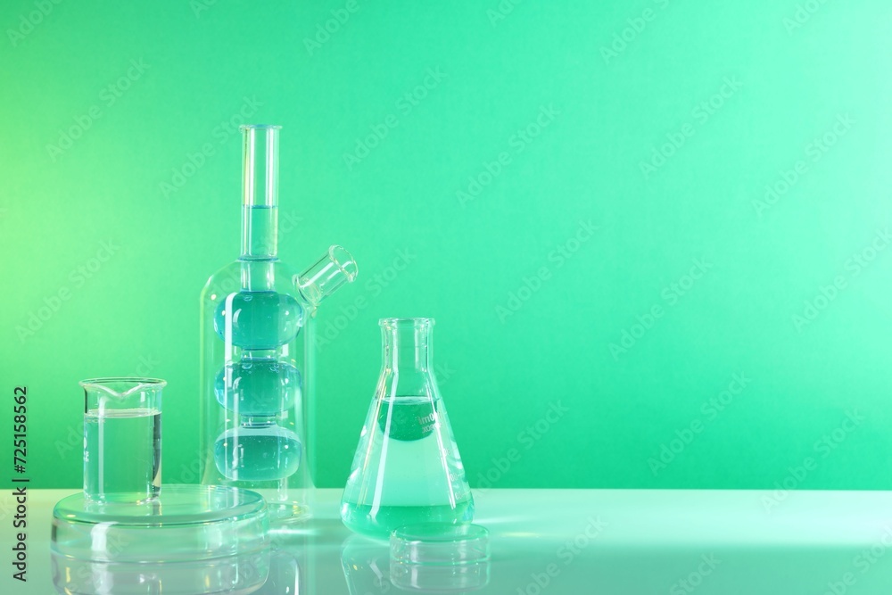Laboratory analysis. Different glassware on table against green background, space for text Laboratory analysis. Different glassware on table against green background, space for text