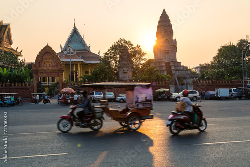 Tuk tuk and motorbikes in the street at sunset, Phnom Penh, Cambodia photo