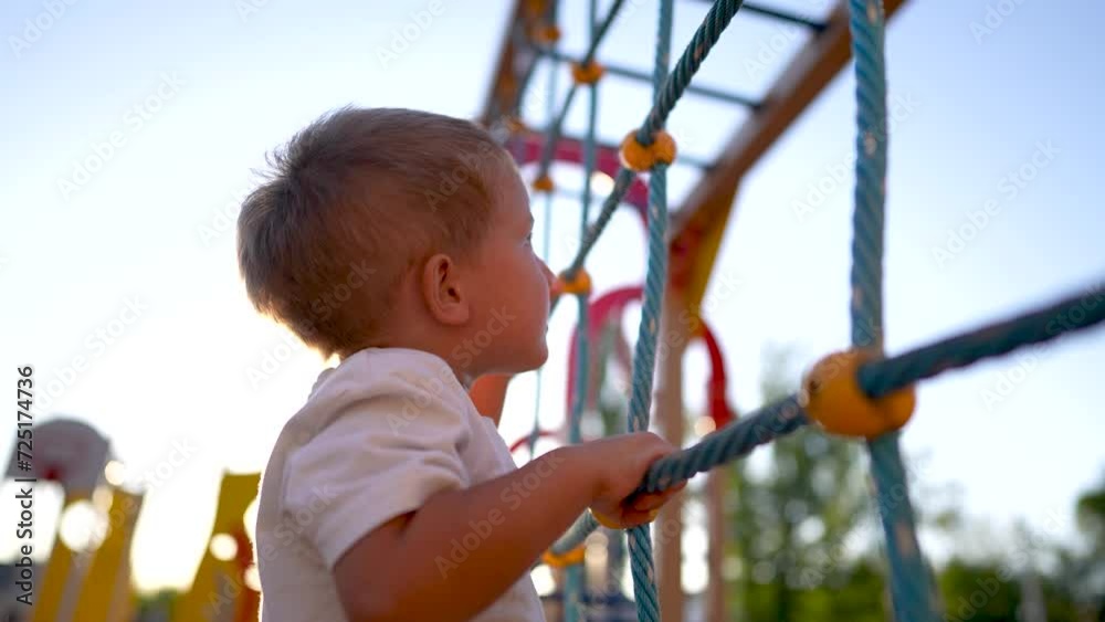 child plays on the playground. concept of a happy childhood and loving family. a child smiles joyfully and climbs a ladder on a playground, lifestyle the glare of the sun in the background child plays on the playground. concept of a happy childhood and loving family. a child smiles joyfully and climbs a ladder on a playground, lifestyle the glare of the sun in the background