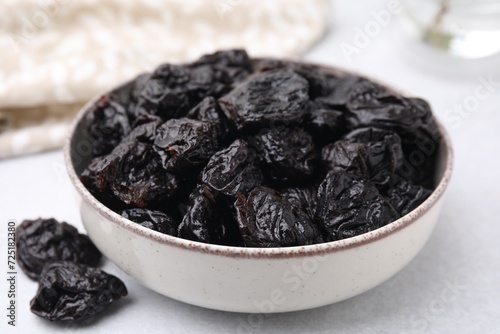 Bowl with sweet dried prunes on light table, closeup