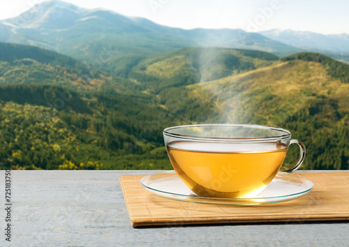 Aromatic green tea in glass cup on grey wooden table in mountains, space for text