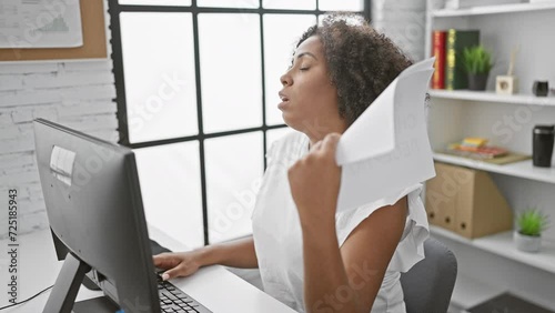 Black woman using paper as fan in modern office photo