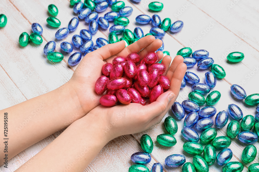 Female hands full of chocolate Easter eggs on light wooden background, closeup