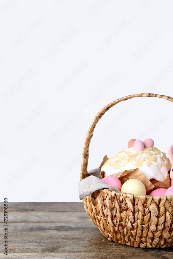 Basket with Easter eggs and cake on wooden table against grey background