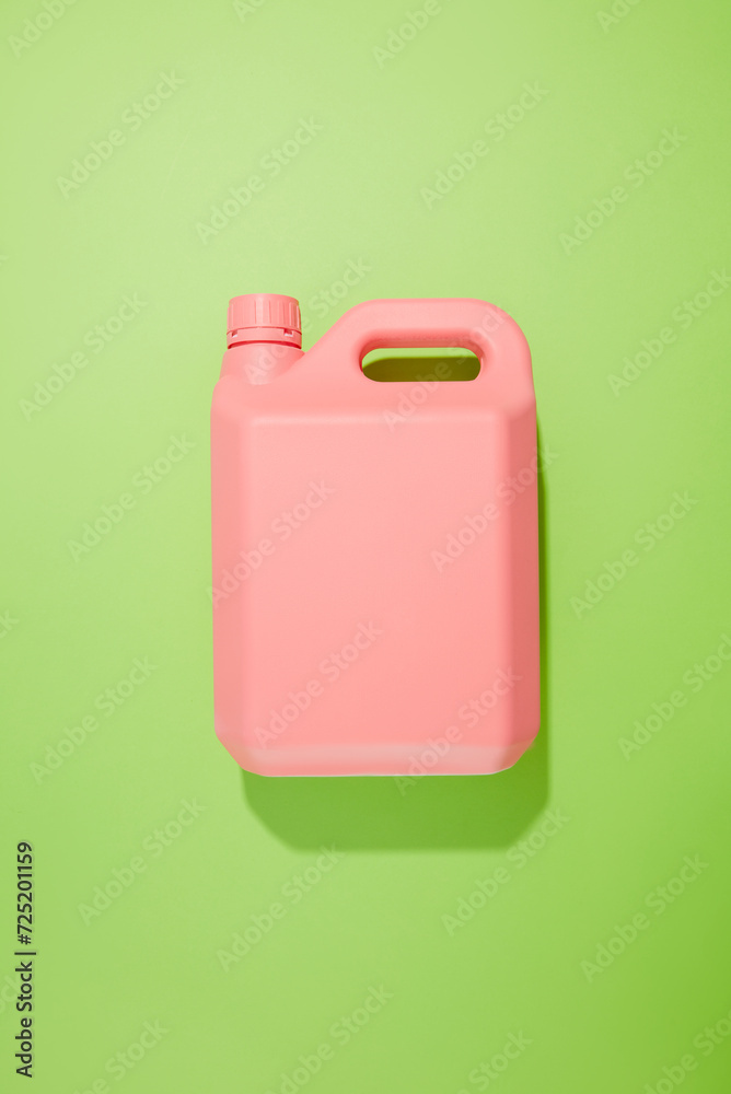 On a green background, a pink plastic canister of detergent without a label isolated. Blank space for design. Minimal scene for advertising. Cleansing product On a green background, a pink plastic canister of detergent without a label isolated. Blank space for design. Minimal scene for advertising. Cleansing product