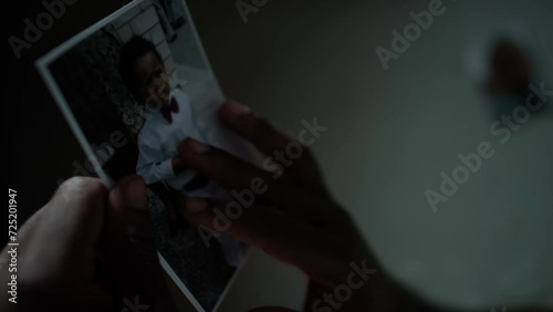Close up shot of African American inmate lying on bed in prison cell, watching photo of baby son and missing him photo