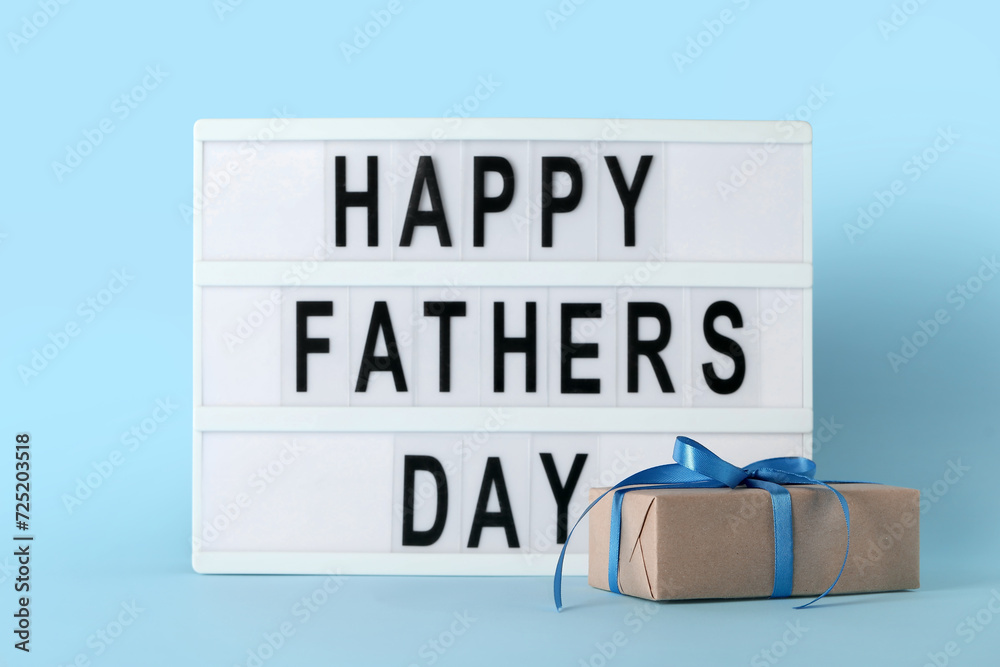 Board with text HAPPY FATHER'S DAY and gift on blue background