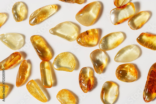 Amber stones at sunlight on light background, stone yellow beige color. Natural gemstone mineral material, healing crystal. Top view Amber texture. Nature gems, pieces ancient resin.