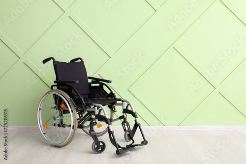 Modern empty wheelchair near green wall