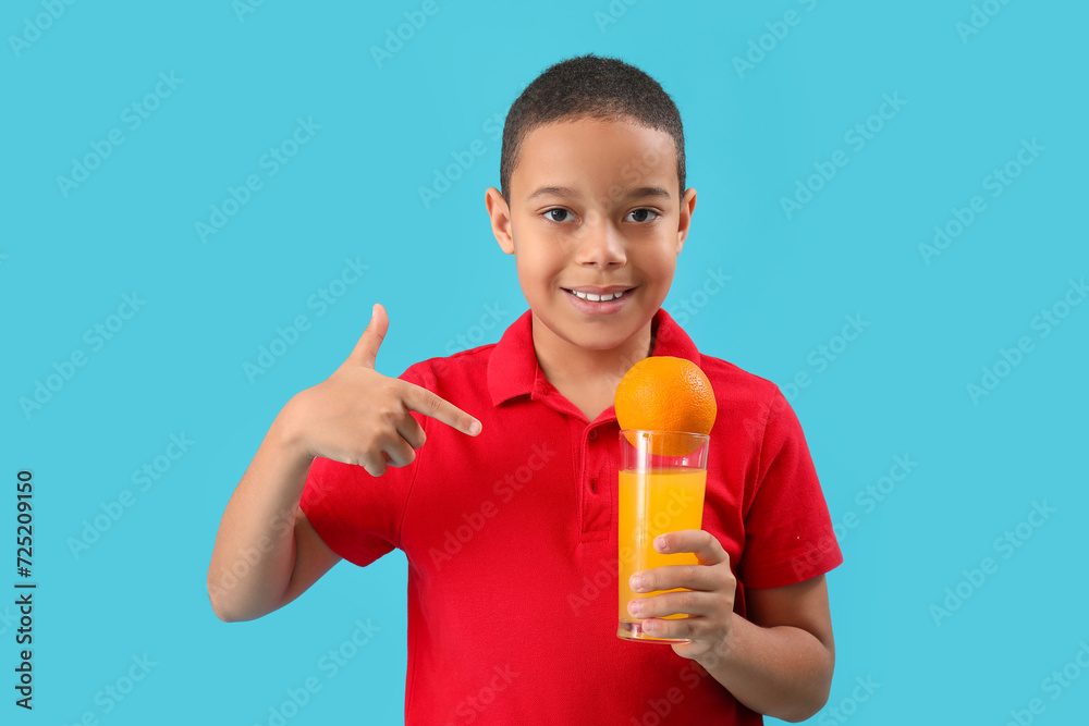 Little African-American boy pointing at glass of juice and orange on blue background Little African-American boy pointing at glass of juice and orange on blue background