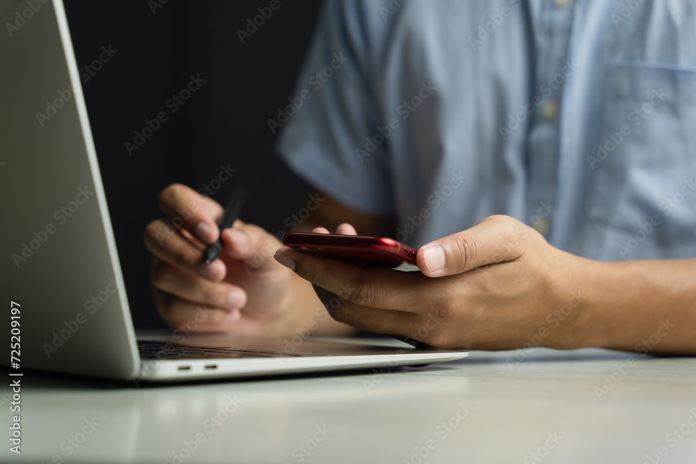 Fototapeta premium A man in a blue shirt uses a smartphone or tablet in a dark room. Holding hands. Black background. Home office. For work. For social media or searching for information