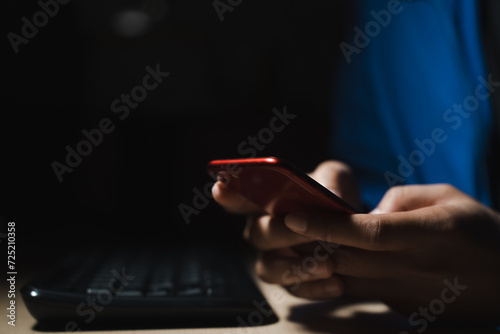 A man in a blue shirt uses a smartphone or tablet in a dark room. Holding hands. Black background. Home office. For work. For social media or searching for information