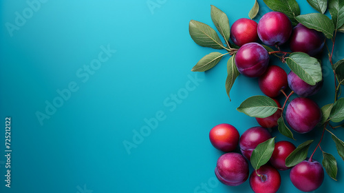 Vibrant red plums with fresh green leaves arranged asymmetrically on a teal background, emphasizing a healthy and organic food concept, copyspace photo