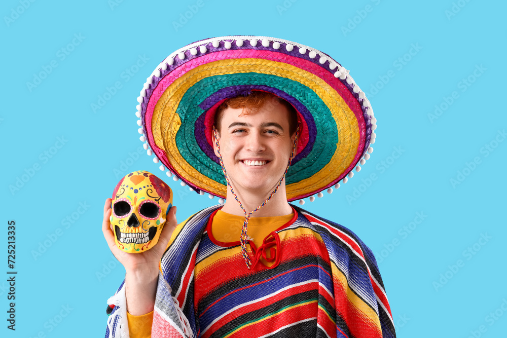 Young Mexican man in sombrero and with painted skull on blue background. Celebration of Day of the Dead Young Mexican man in sombrero and with painted skull on blue background. Celebration of Day of the Dead