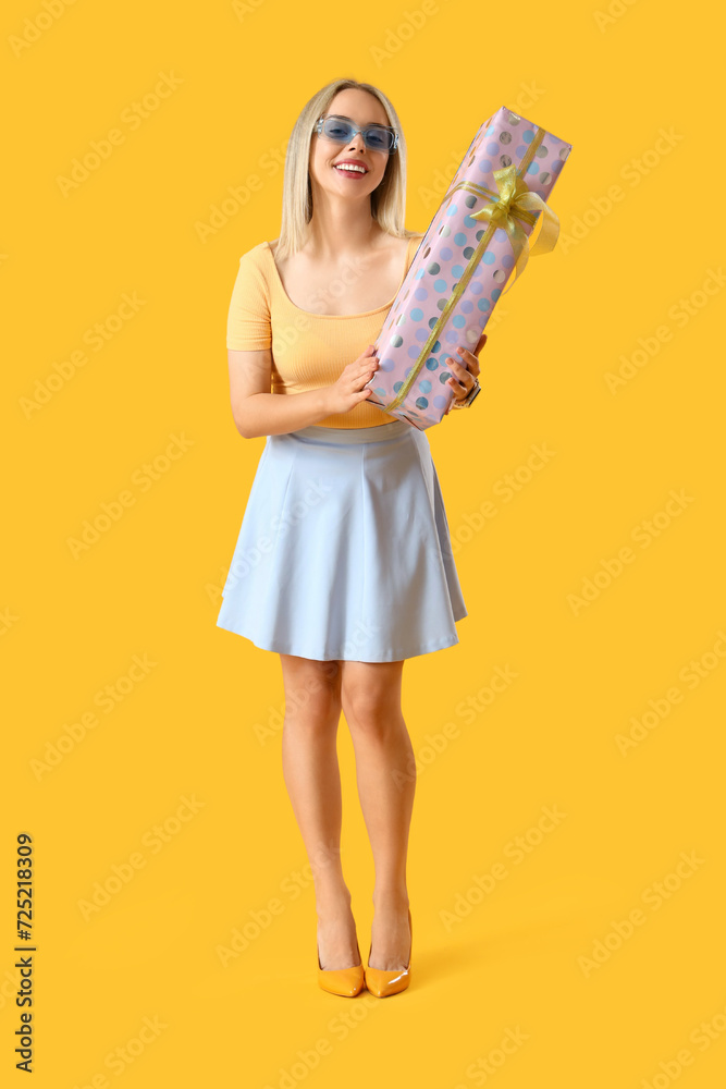 Beautiful young stylish woman with gift box on yellow background Beautiful young stylish woman with gift box on yellow background