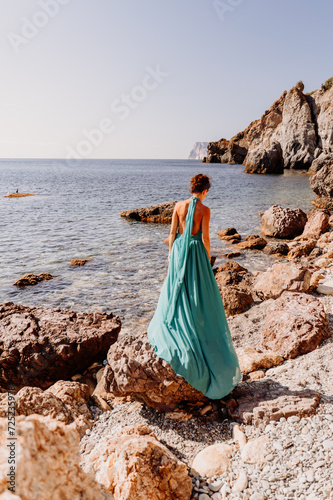Woman green dress sea. Woman in a long mint dress posing on a beach with rocks on sunny day. Girl on the nature on blue sky background.