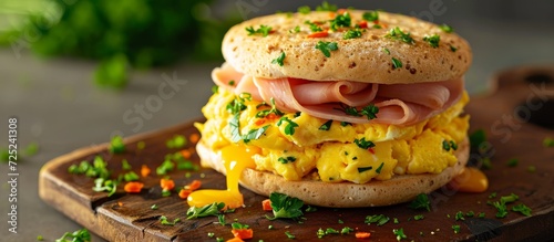 Breakfast sandwich with English muffin, scrambled egg, ham, and cheese, placed on a cutting board. photo