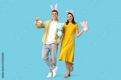 Happy young couple with Easter bunny ears  basket and gifts on blue background