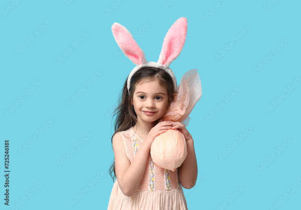 Cute little girl in bunny ears with Easter gift egg on blue background Cute little girl in bunny ears with Easter gift egg on blue background