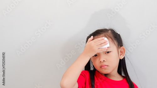 Little Asian girl holding tissue paper on forehead, feel sick and fever.