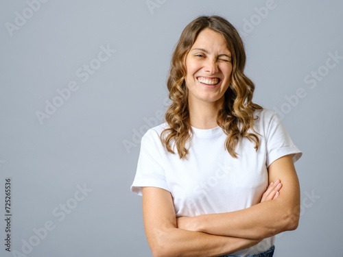 Cheeky woman smiling and winking at camera with confidence, cross arms on chest
