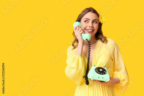 Young woman talking by retro telephone with beautiful chrysanthemum flower on yellow background. International Women's Day