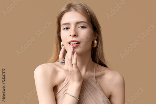 Beautiful young woman with stylish jewelry on brown background