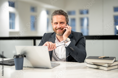 Modern office. Successful caucasian business man in business suit using laptop, working remotely, e-commerce online at office. Finance auditor. Business man talking on phone at office workplace.