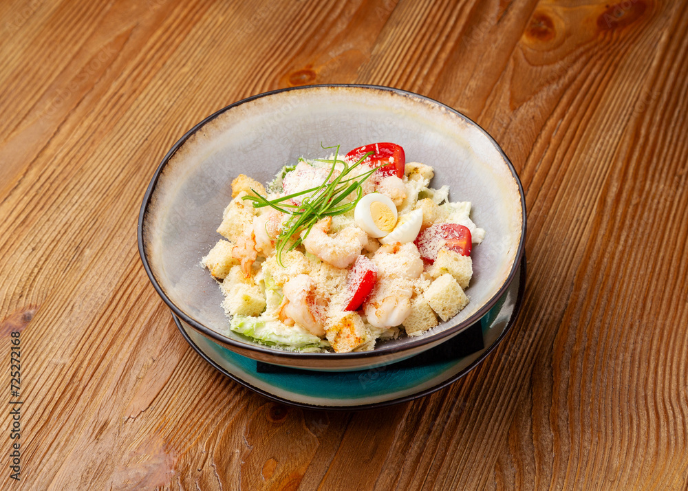 Caesar salad with shrimp in a plate on a wooden background Caesar salad with shrimp in a plate on a wooden background