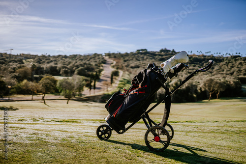 Sotogrante, Spain - January 25, 2024 - Golf bag on a trolley against a scenic golf course backdrop with trees and a clear sky.