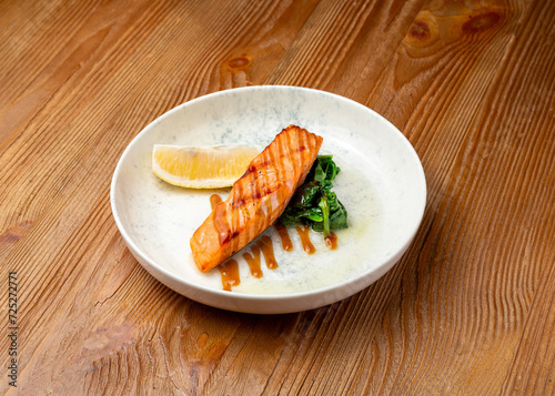 Grilled salmon with spinach and lemon on a plate on a wooden background