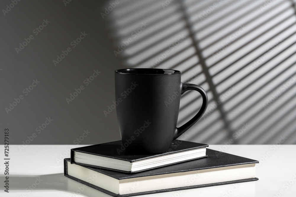 Black cup on books in sunlight on gray background Black cup on books in sunlight on gray background