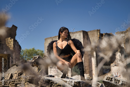 South American woman, young, beautiful, brunette with lingerie and black wings, posing crouching seen through some dry plants in the middle of the ruins of a building. Concept angels, beauty, costumes