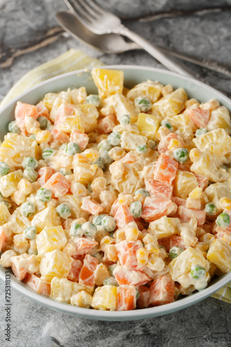 Brazilian gaucho salad is made with a combination of potatoes, carrots, peas, corn, thinly sliced green apples and mayonnaise closeup on the plate on the marble table. Vertical