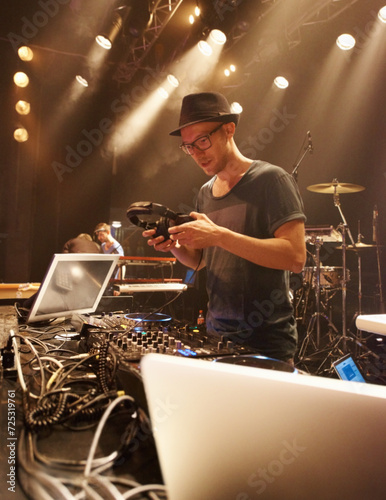 Music, DJ and spotlight on man at stage with headphones and equipment for performance on sound board. Techno, musician and person in club at night mixing on turntable with technology for rave
