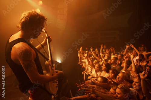 Guitar, concert and crowd at stage with man in performance of rock, metal and music. Festival, event and audience of people in celebration of talent in theater at night with spotlight and energy
