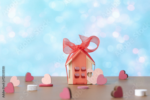 House model with red bow and decorative valentines hearts over holiday defocused lights. Valentine’s day concept