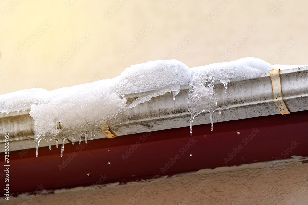 Snow and icicles melting on roof. Risk of snow sliding off building roof. Clogged gutter freeze in winter, ice dams
