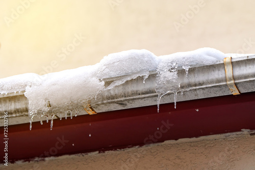 Snow and icicles melting on roof. Risk of snow sliding off building roof. Clogged gutter freeze in winter, ice dams