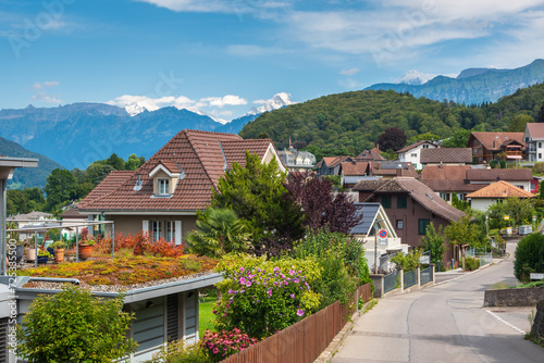 Street view of beautiful houses with flowers and greenery  mountains in the background  the town of Spiez  Swiss Alps  Switzerland.    