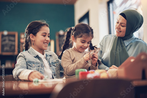 Smiling muslim mother wearing a hijab doing a family arts and crafts with her two young daughters during a weekend activity together photo