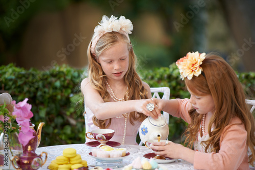 Playing, tea party and girl children in garden for pretend with cake, flowers or kid fun. Princess, cookies and fantasy with friends, teapot and backyard with celebration, imagination and drink.