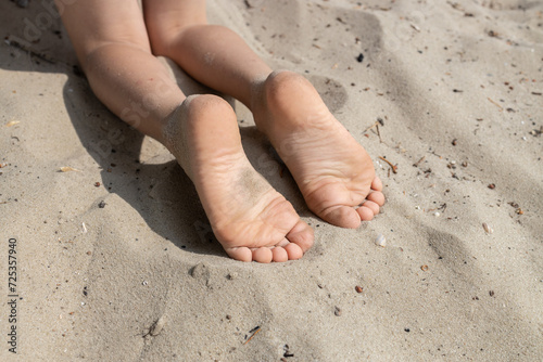 The child's bare feet lie on the warm sand. Carefree childhood, the joy of summer. holidays and healthy lifestyle concept. Healthy feet, lovely toes. © Anna