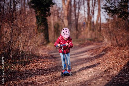 Child in a helmet focused on riding a scooter along a forest trail, adventure time outdoors
