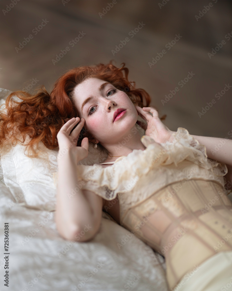 A girl with long red hair in a lace chemise with a corset lies on the bed A girl with long red hair in a lace chemise with a corset lies on the bed