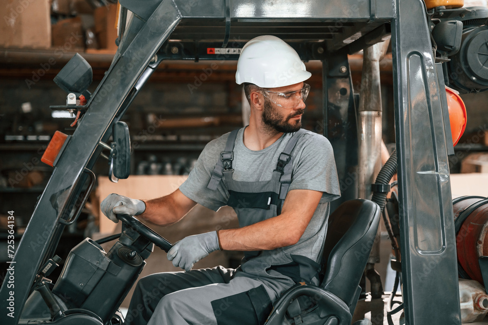 Driving the forklift. Young factory worker in grey uniform Driving the forklift. Young factory worker in grey uniform